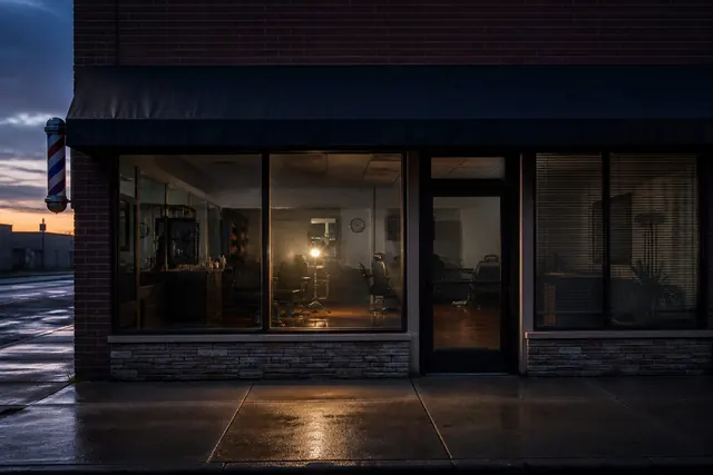 A closed barbershop storefront at dusk with one work light still on.